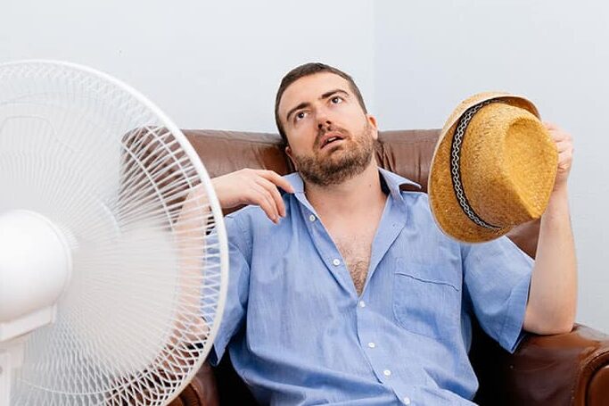man sitting in front of fan because AC is broken