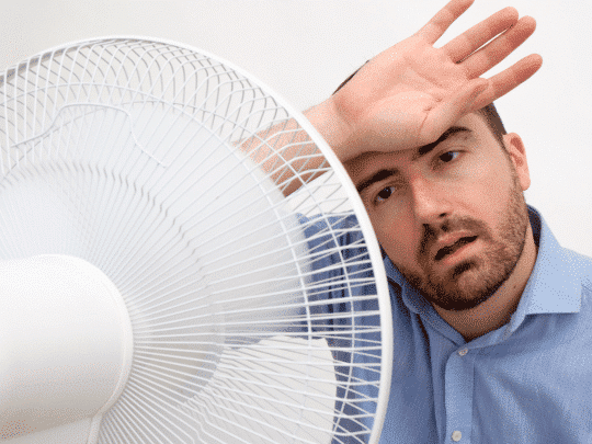 man sitting in front of fan, trying to cool down because his AC is broken